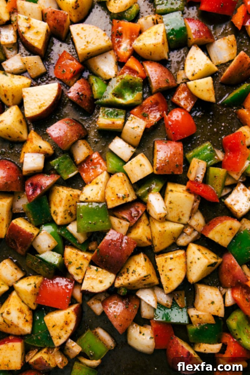 A full shot of the sheet pan filled with seasoned red potatoes, bell peppers, and onions, ready for roasting.