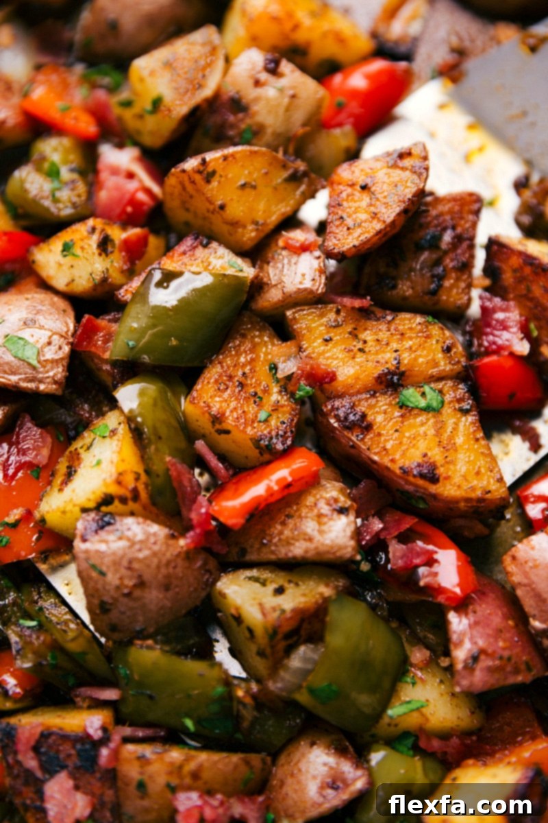 Close-up of a large sheet pan with roasted breakfast potatoes, bell peppers, and onions, being tossed with a spatula.