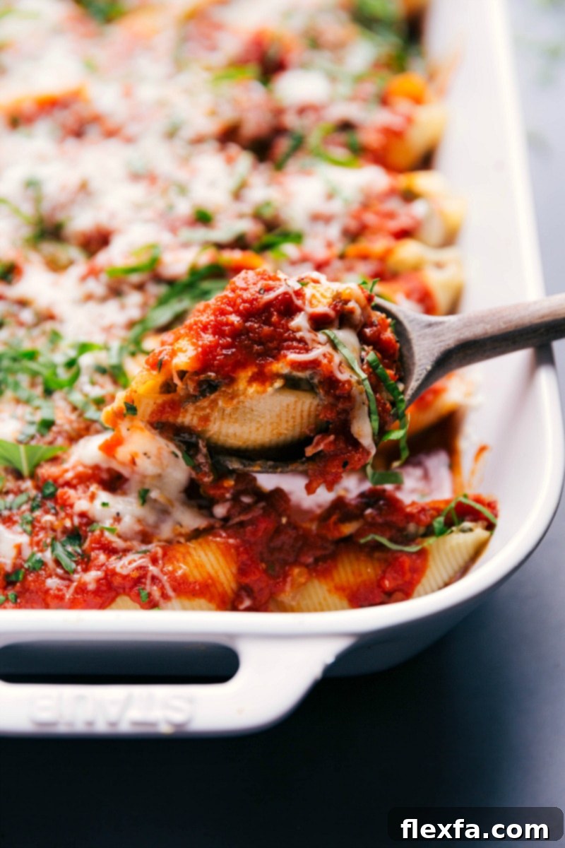 A serving spoon scooping out a hearty portion of savory stuffed shells with italian sausage from a baking dish.