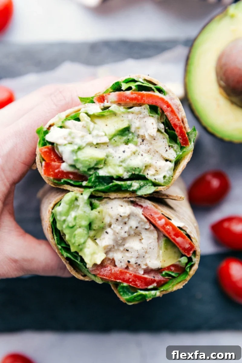 Our absolute favorite chicken salad made in wrap form A deliciously cut open Chicken Salad Wrap showing the rich filling of chicken salad, tomatoes, avocado, and lettuce.