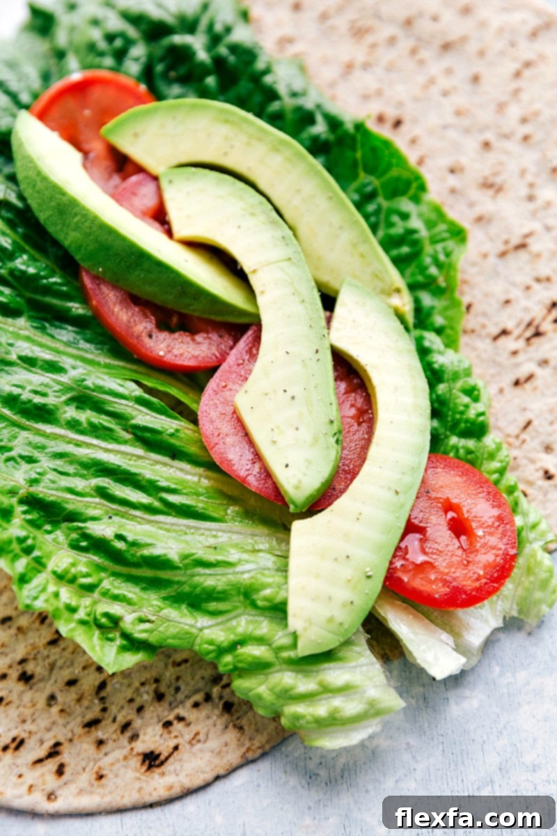 Our absolute favorite chicken salad A whole wheat tortilla layered with fresh romaine lettuce, sliced Roma tomatoes, and creamy avocado, ready for the chicken salad filling.