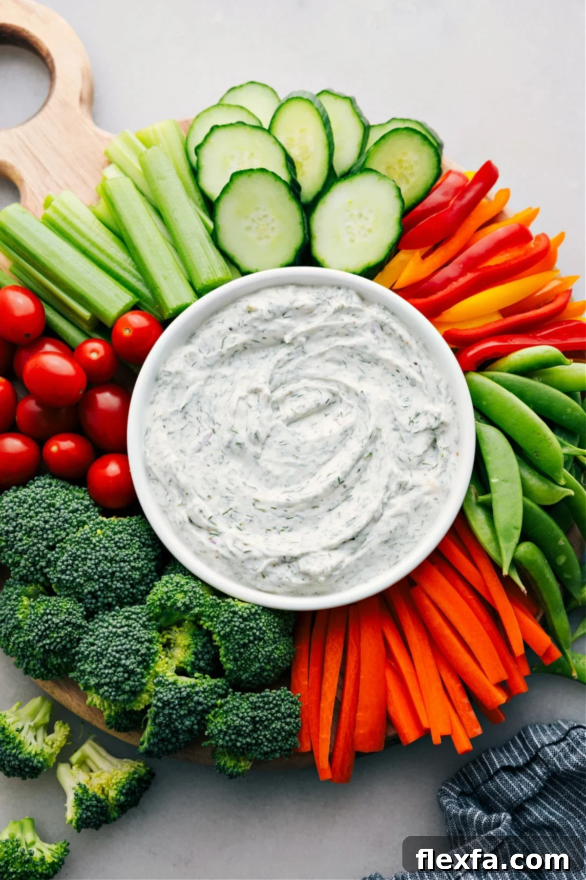 A beautifully composed platter showcases a central, inviting bowl of creamy homemade veggie dip. It's surrounded by an abundant and colorful assortment of fresh, crisp vegetables, meticulously arranged. These include vibrant bell pepper strips, perfectly cut crunchy carrot sticks, refreshing cucumber slices, and juicy cherry tomatoes, all set for a delightful and healthy snacking or hosting experience.