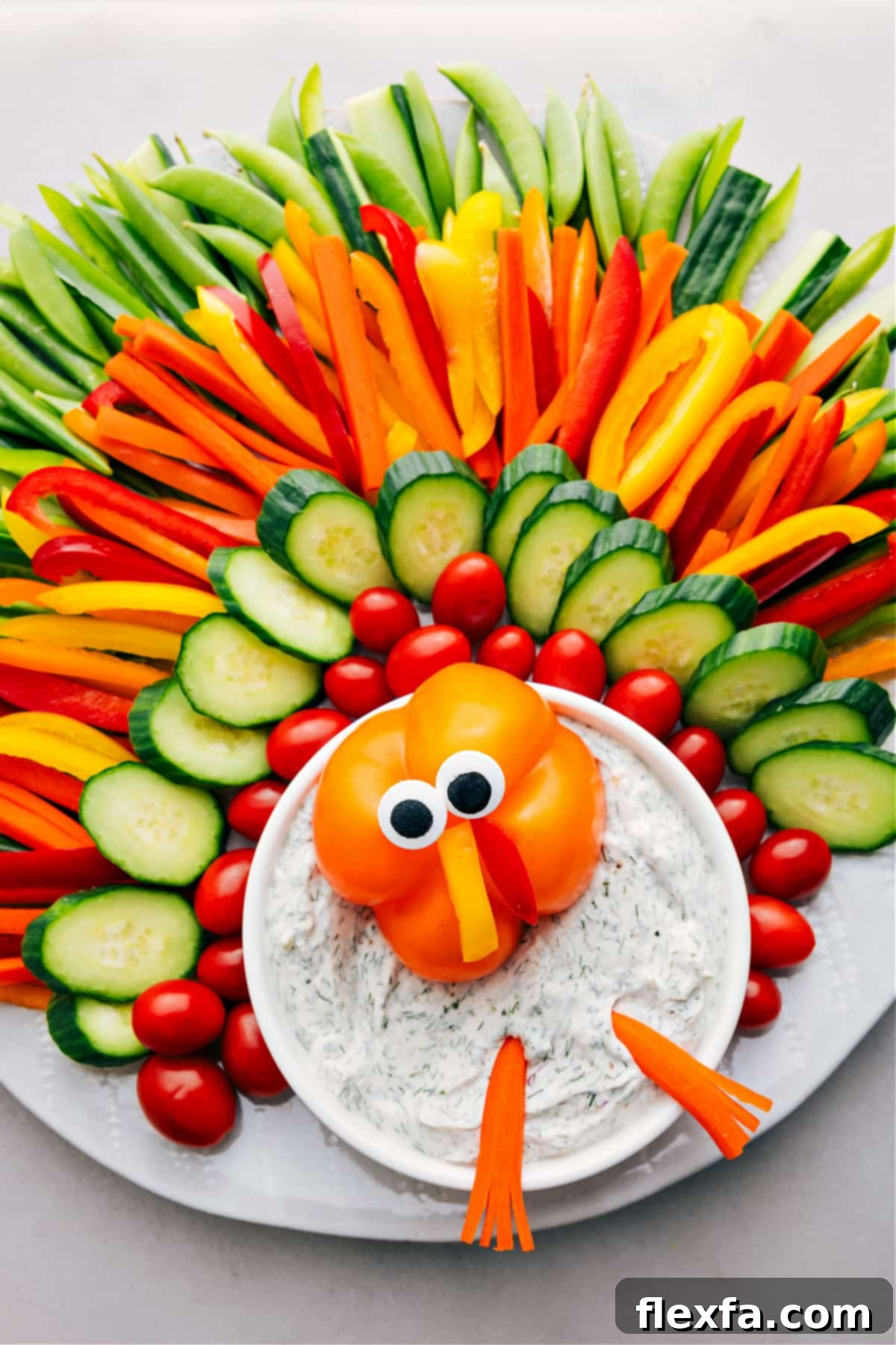 An array of colorful vegetables ingeniously arranged on a platter to resemble a festive turkey, making for an adorable and healthy Thanksgiving appetizer. The design features various bell peppers, crisp cucumber slices, tender snap peas, and a central bowl of creamy dip.
