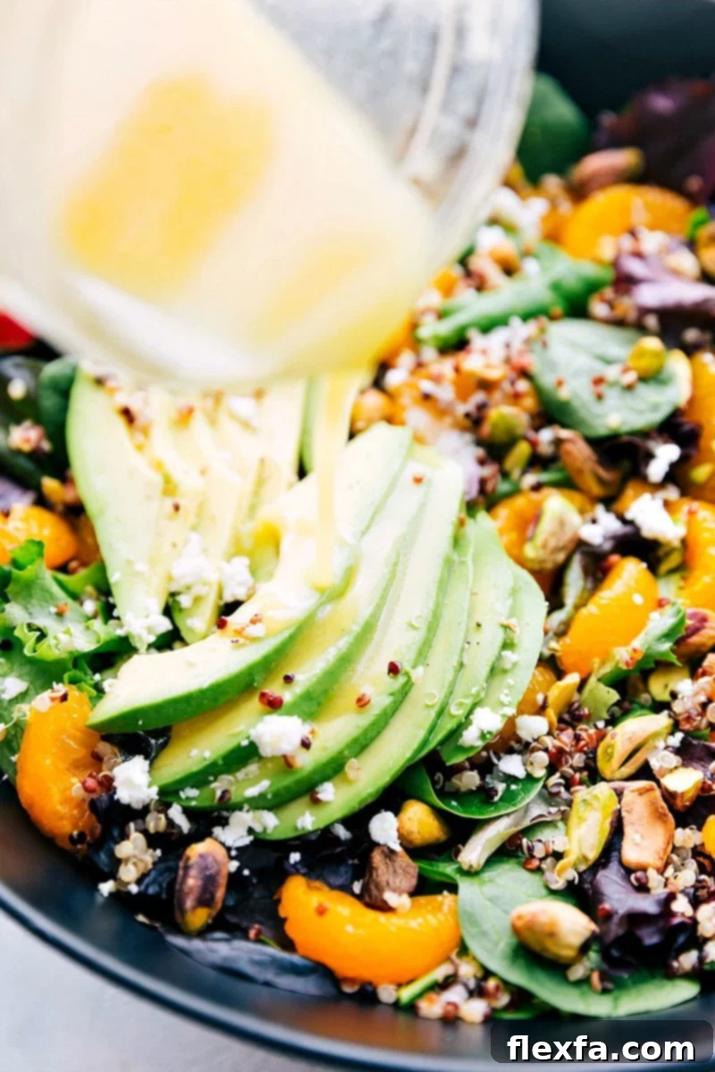 A close-up image showing a stream of vibrant, tangy citrus vinaigrette being generously poured over a beautifully assembled Citrus Quinoa Salad, highlighting the appealing textures of the fresh ingredients and the glistening dressing.