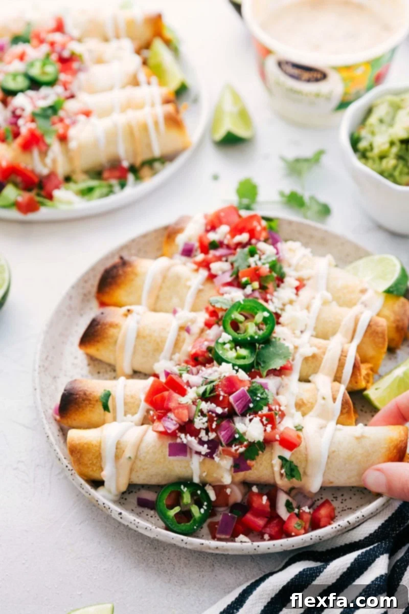 Close-up of golden brown baked chicken taquitos lined up on a baking sheet, glistening with cooking spray, ready to be baked.