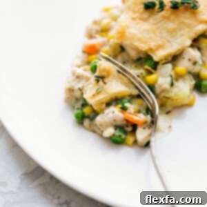 A savory and flavorful chicken pot pie on a white plate, with a bite taken out to reveal its creamy filling, golden crust, and vibrant vegetables. Served as a comforting meal.