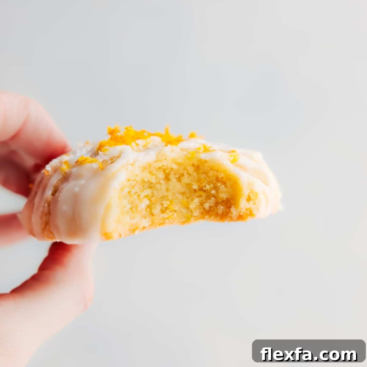 Stack of lemon cookies with glaze, garnished with fresh lemon zest, on a rustic background.