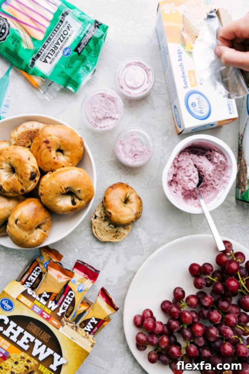 A healthy school lunch, including bagels, string cheese, cream cheese, grapes, and granola bars, arranged for easy packing.