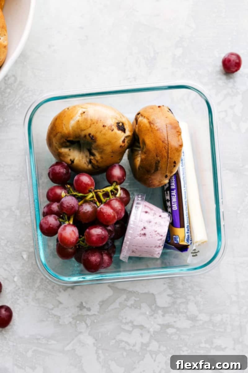 A bagel with a side of cream cheese, fresh grapes, and string cheese in a container, ready to go.