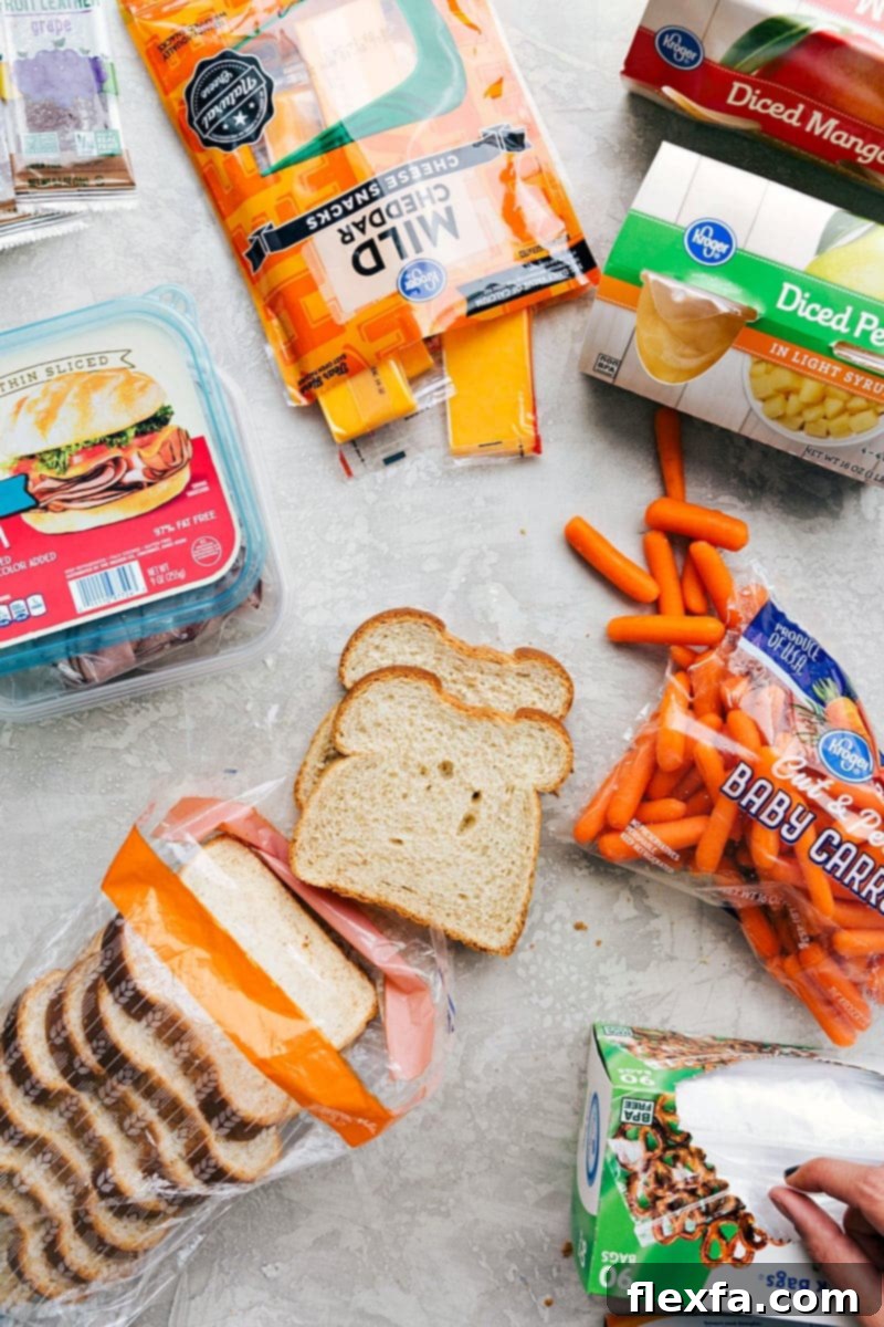 Sliced deli meat, cheese, fruit, bread, veggies, and a fruit snack, all packed together for a nutritious and balanced school lunch idea for kids.