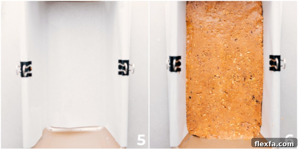 The protein bar mixture being firmly pressed into a bread pan lined with parchment paper, ensuring an even and compact base.