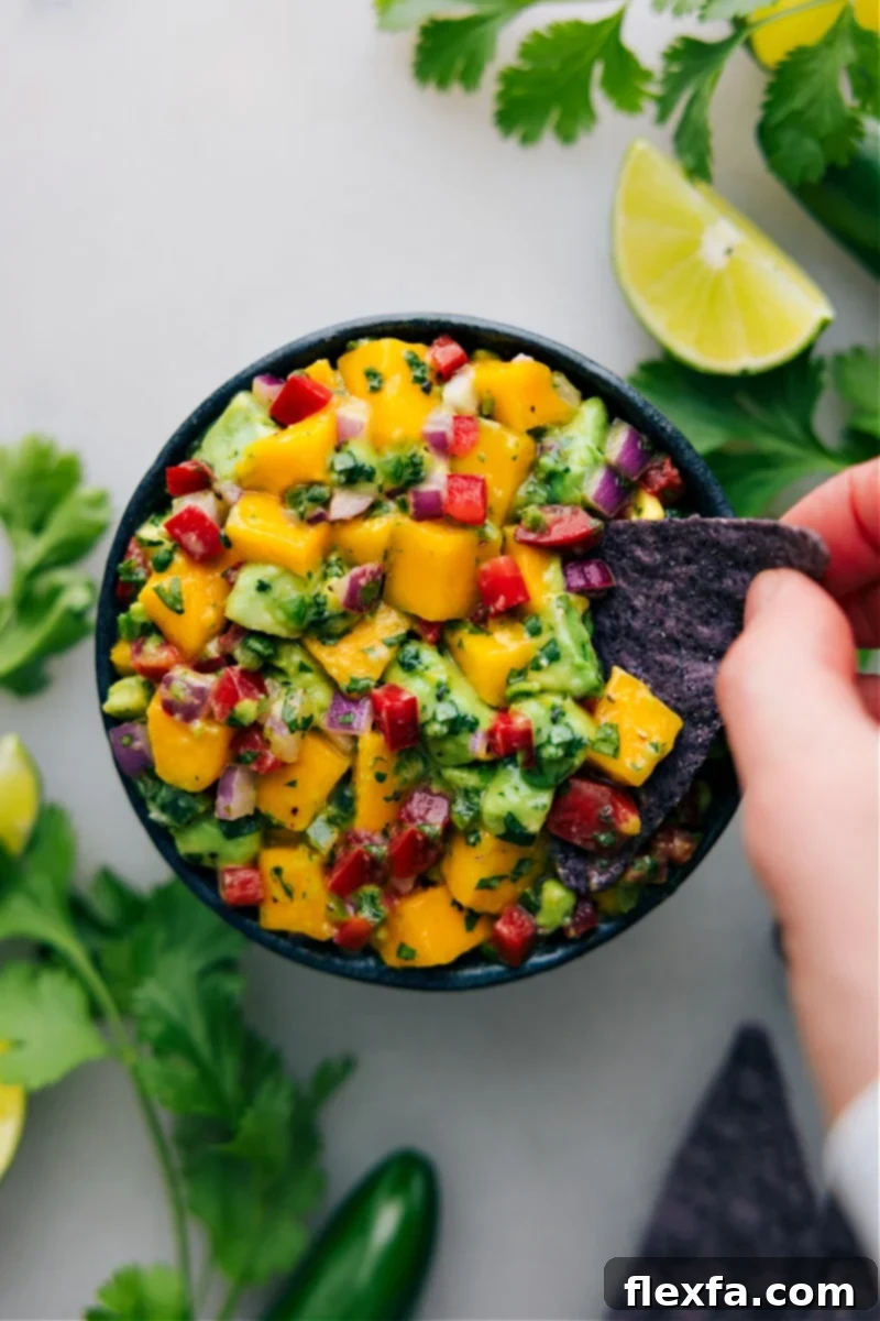 Overhead image of a tortilla chip dipping into a bowl of fresh Mango Salsa, highlighting its vibrant texture.