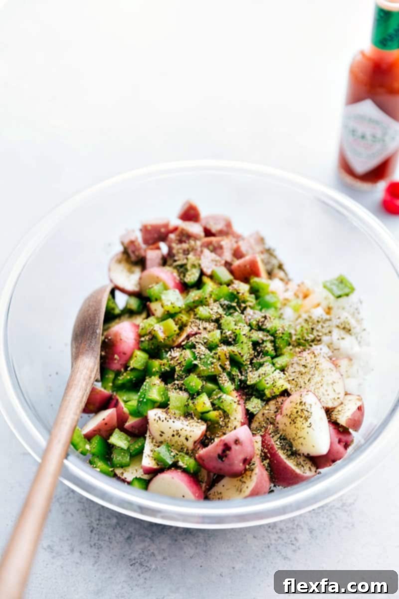 All the veggies, sausages, and seasonings added to a large bowl, ready to be tossed together before packing into foil.