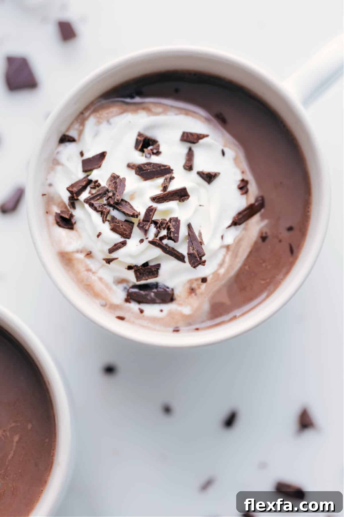 A rich mug of homemade hot chocolate, beautifully topped with a swirl of fluffy whipped cream and delicate chocolate shavings, inviting warmth and indulgence.