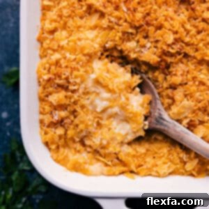 A close-up shot of a serving of Funeral Potatoes in a white dish, showcasing the golden-brown crispy topping and creamy, cheesy interior.