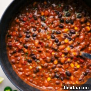 Close-up of a bowl of hearty vegetarian chili, garnished with cheese, sour cream, and fresh cilantro.