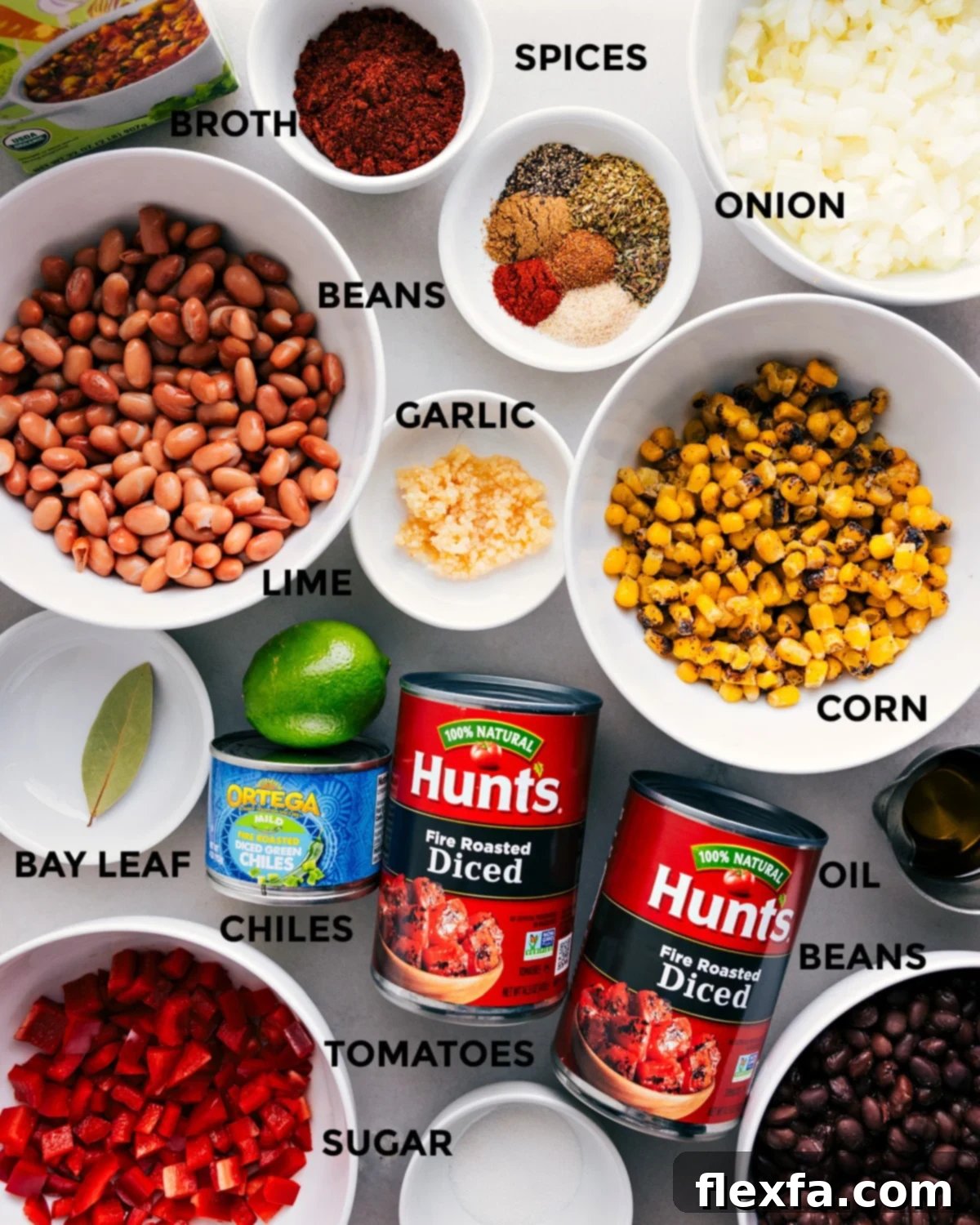 All the fresh ingredients for vegetarian chili are prepped and neatly arranged on a cutting board, including spices, various vegetables, different types of beans, minced garlic, fresh lime, vegetable broth, diced tomatoes, green chiles, olive oil, and a bay leaf, ready for easy assembly.