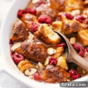 Scooping golden Croissant Breakfast Bake with visible chunks of bread, drizzled syrup, and fresh raspberries, topped with a dollop of whipped cream for a perfect finish.