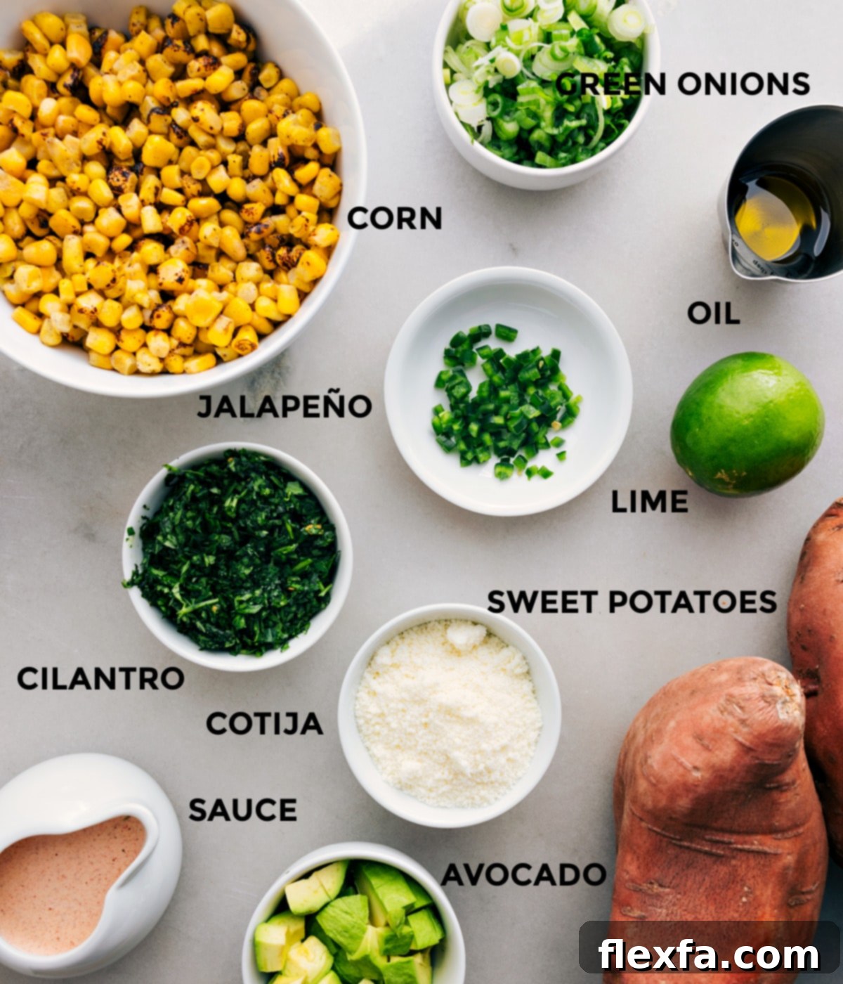 All the fresh ingredients for Mexican street corn loaded sweet potatoes are prepped and ready for assembly, including corn, green onions, avocado, lime, jalapeño, cilantro, cotija cheese, and the creamy sauce components.