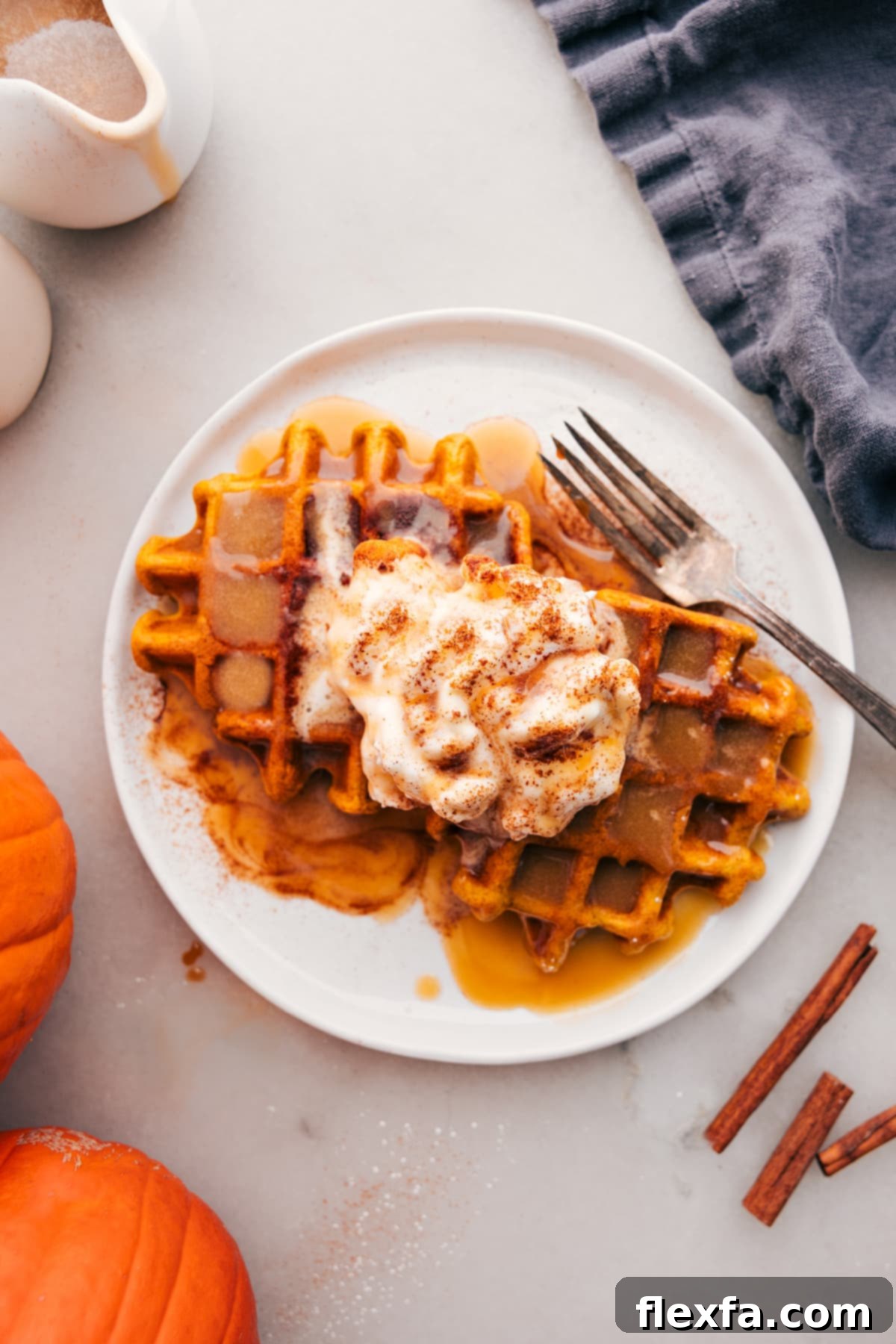 Golden pumpkin waffles stacked, drizzled with maple syrup and topped with fresh whipped cream, ready to be served for breakfast.
