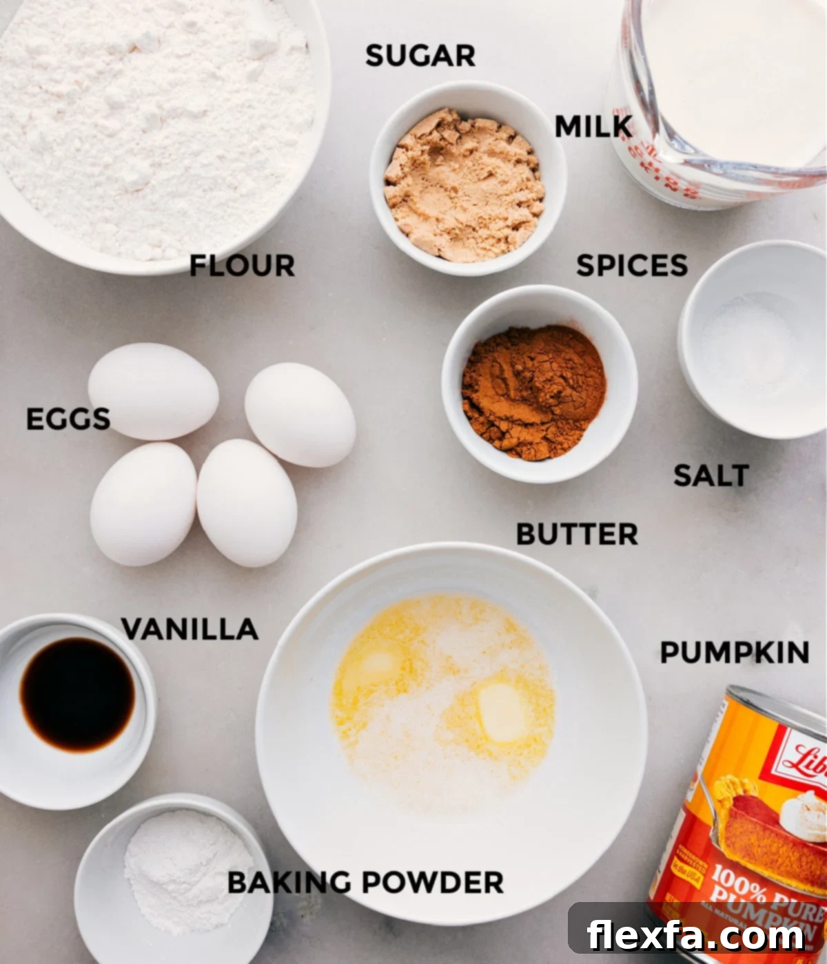 All the essential ingredients for pumpkin waffles laid out on a table, including flour, sugar, milk, spices, salt, melted butter, eggs, pumpkin puree, vanilla extract, and baking powder.