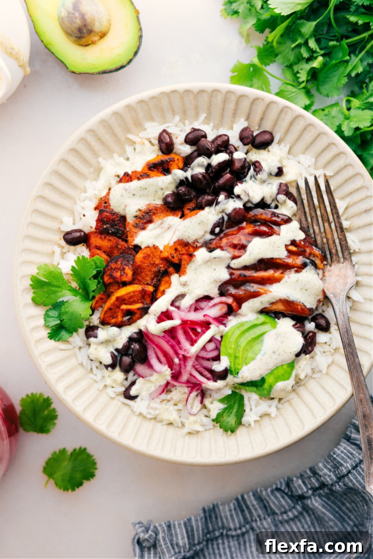 Easy And Delicious BBQ Chicken Rice Bowls A beautifully arranged BBQ Chicken Bowl ready to be served, featuring a base of rice, tender BBQ chicken, roasted sweet potatoes, black beans, diced avocado, and vibrant pickled red onions, topped with a drizzle of green goddess dressing.