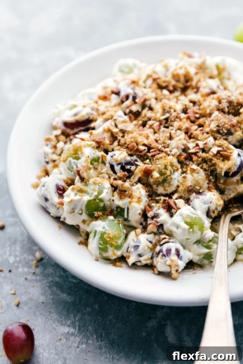 Delicious Creamy Grape Salad Ready to Serve A serving bowl of Grape Salad with a spoon, showing off its creamy texture and crunchy pecan topping, ready to be enjoyed.