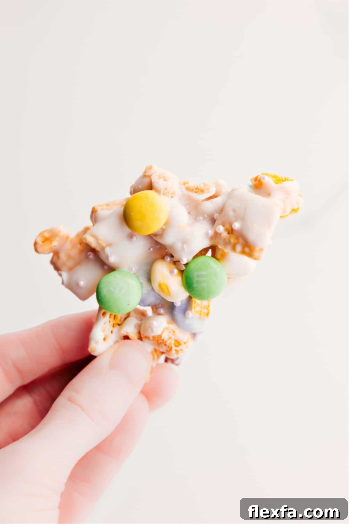 Enjoying a Piece of Delicious Bunny Bait A hand holding up a piece of Bunny Bait, showcasing its crunchy texture and colorful M&M's, ready to be enjoyed.