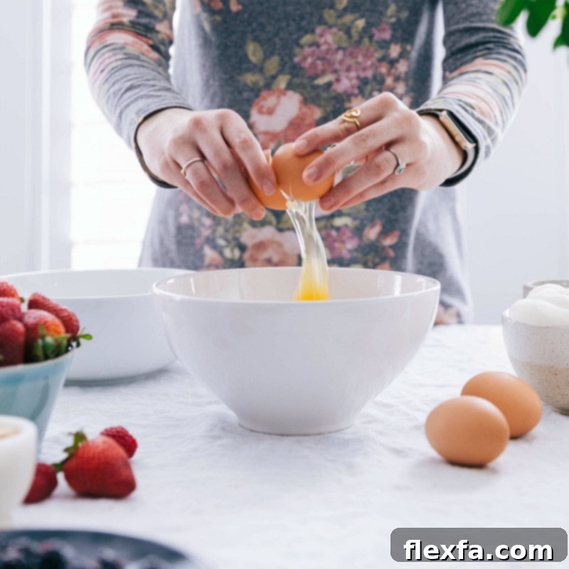 An egg being carefully cracked into a mixing bowl, symbolizing the start of a fresh homemade waffle recipe.