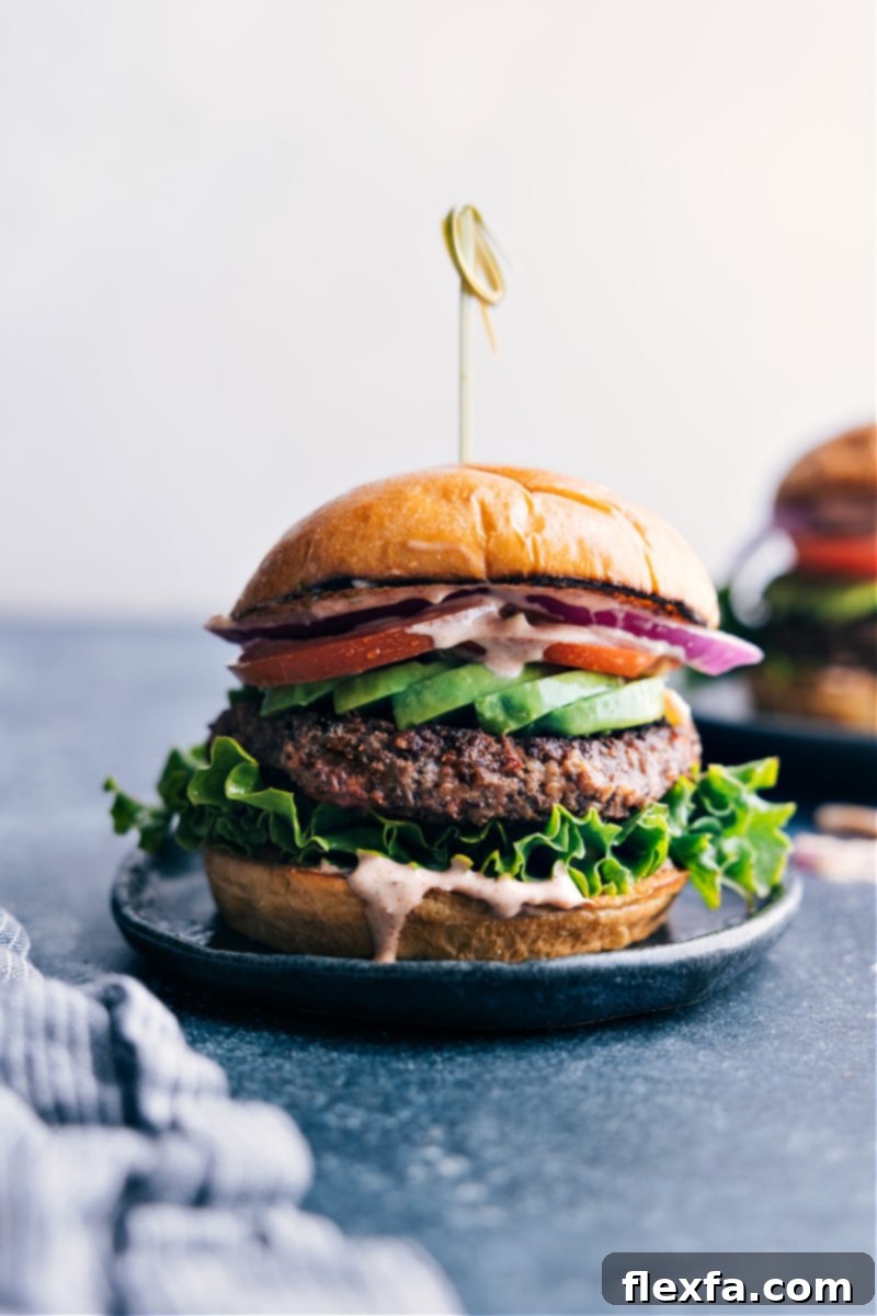 A beautifully assembled black bean burger, richly topped with fresh lettuce, vibrant red tomato, thinly sliced purple onion, and a generous drizzle of creamy sauce, all served enticingly on a perfectly toasted bun.