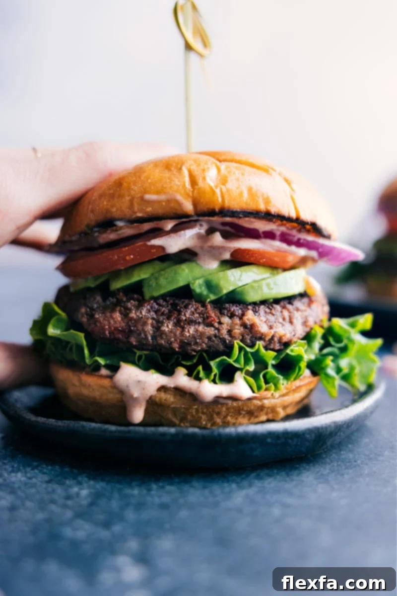A perfectly cooked, gourmet black bean burger, beautifully nestled between a buttery toasted bun and garnished with fresh green lettuce, a vibrant slice of red tomato, and creamy avocado, poised for an irresistible bite.