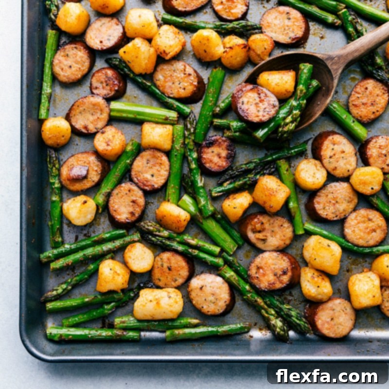 Process shot of the meal roasting on a sheet pan, showing sausage slices, tender asparagus, and golden-brown gnocchi crisping up in the oven.
