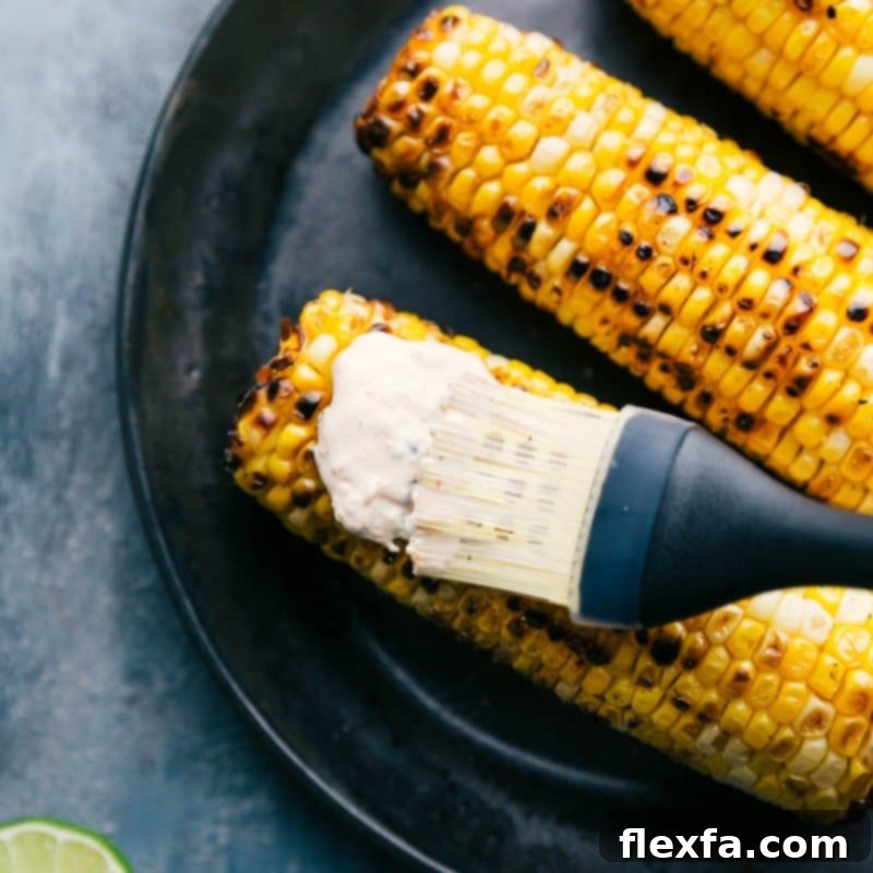Cream sauce being spread on roasted corn with a pastry brush for the elote recipe.