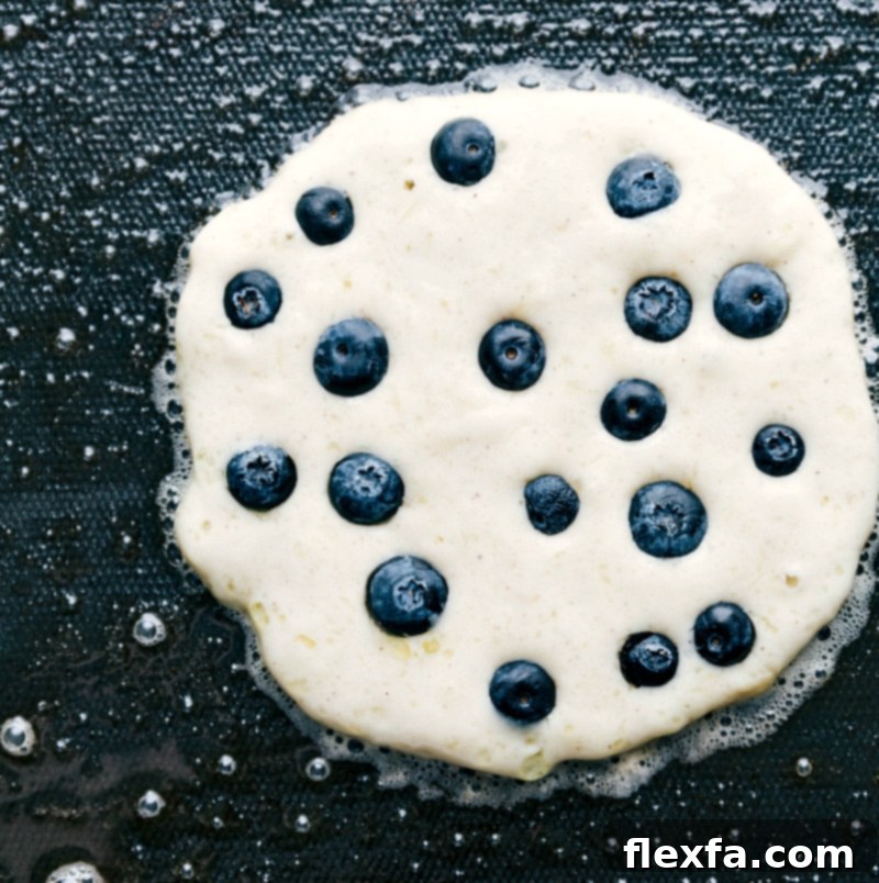 Pancake on the griddle being cooked to a golden brown, with bubbles forming on the surface.