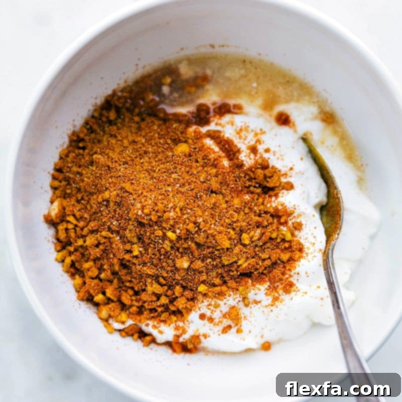 A vibrant flat lay of all marinade ingredients: creamy plain yogurt, bright yellow lemon halves, minced fresh garlic, finely grated ginger, and a selection of colorful ground spices including turmeric, garam masala, cumin, and coriander, all arranged around a mixing bowl ready for combination.