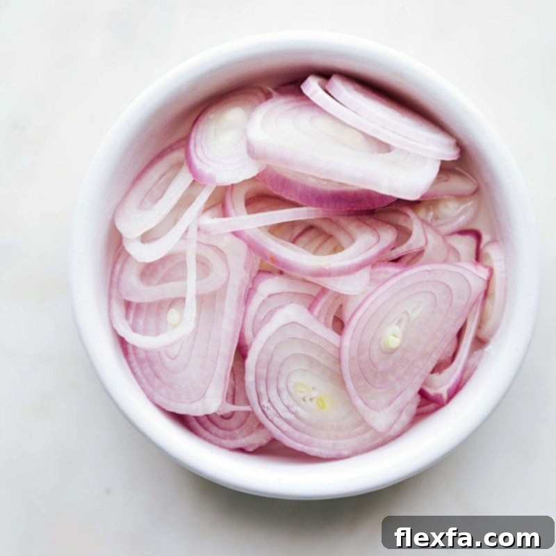 Freshly Sliced Shallots for Topping Fresh shallots finely sliced, ready to be used as a topping for the dish, adding a zesty crunch.