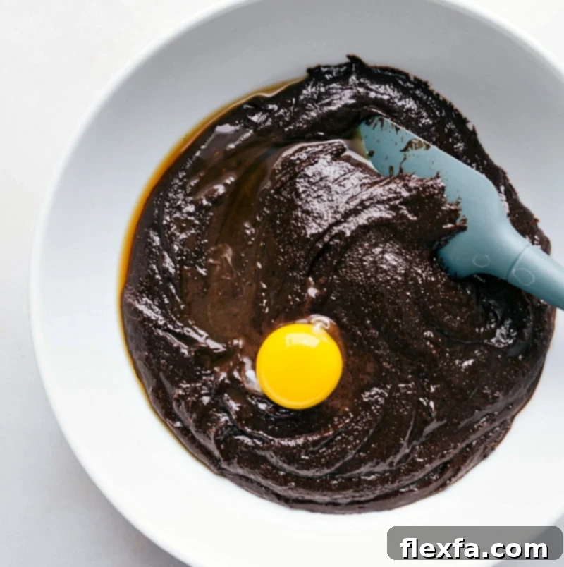 Wet ingredients, including sugar, vanilla, and eggs, being vigorously mixed in a bowl until smooth and fully combined, creating a glossy batter.