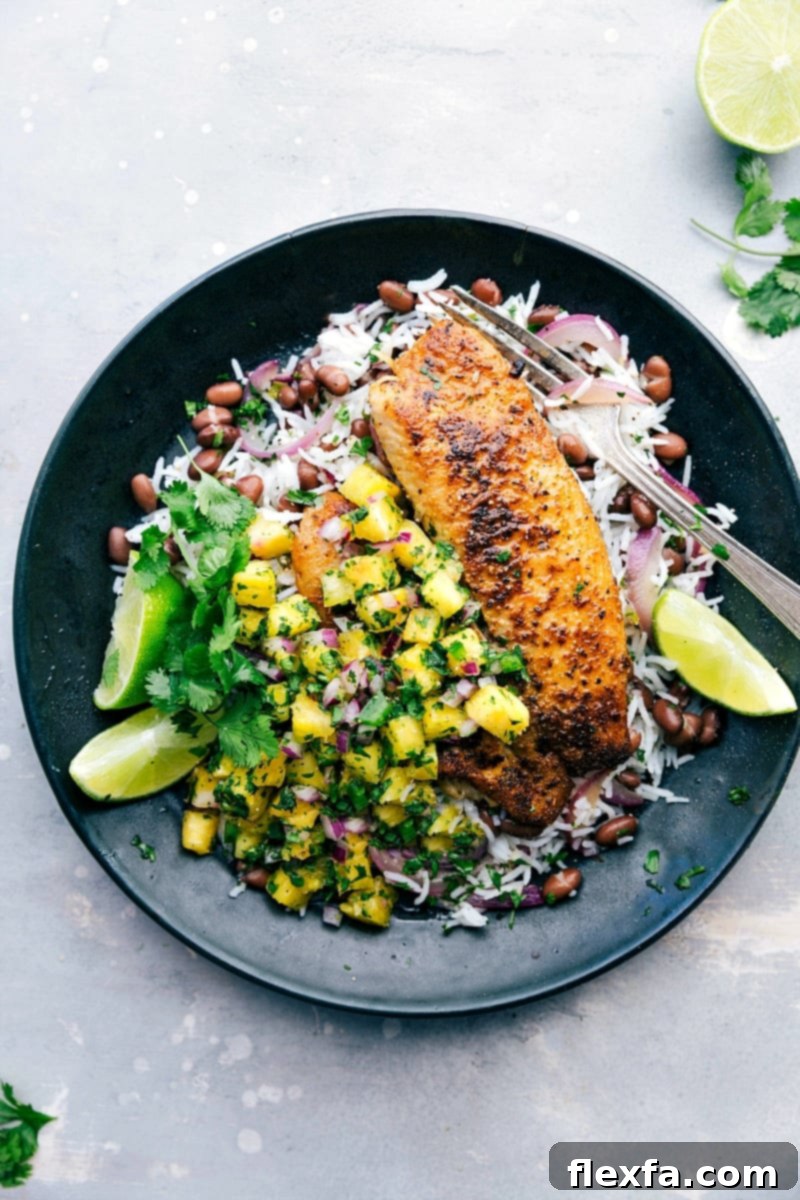 A plate featuring perfectly blackened tilapia served with a vibrant pineapple salsa, alongside fluffy basmati rice, and savory black beans. This healthy and delicious meal is beautifully presented, highlighting the rich colors and textures of each component.