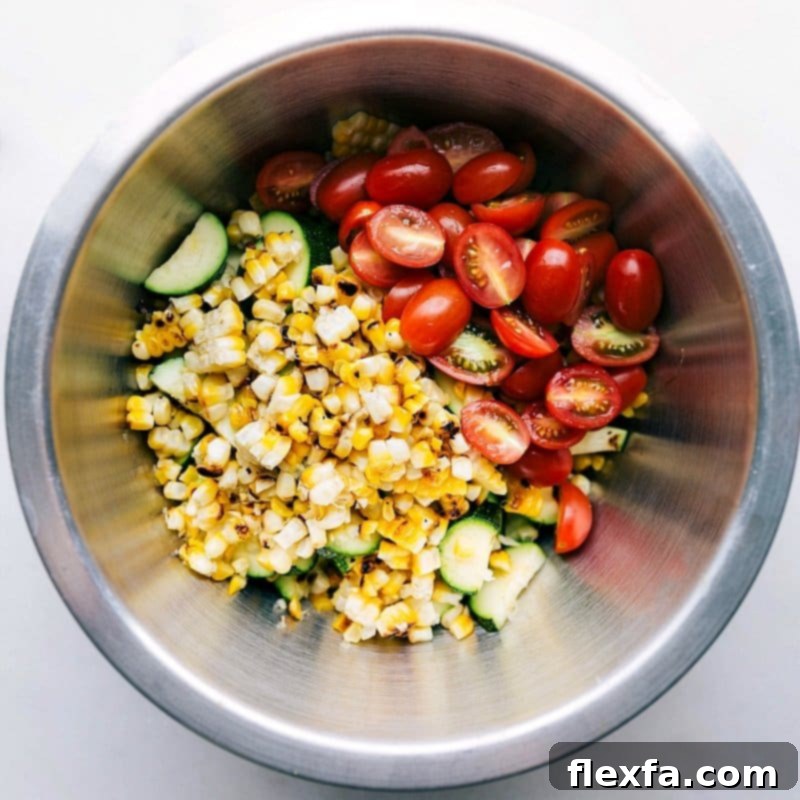 Corn and Zucchini Salad Ready for Mixing A bowl filled with grilled corn and zucchini salad, with the addition of fresh cherry tomatoes and basil, ready for mixing to create a flavorful side dish.