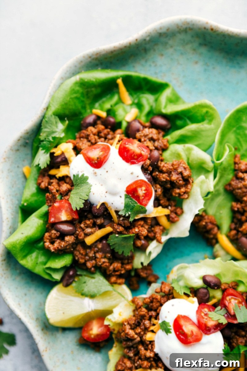 Finished taco lettuce wraps topped with sour cream, cheese, cherry tomatoes, and other toppings, ready for a delightful meal.