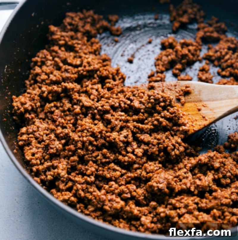 Delicious ground beef cooking in a large cast-iron pan, absorbing the rich flavors of the seasoning blend for a perfectly savory taco filling.