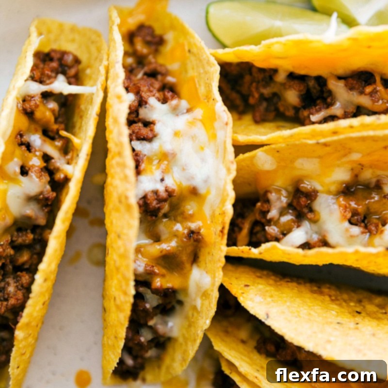 Freshly baked ground beef tacos emerging from the oven, adorned with a generous layer of perfectly melted cheese, steaming hot and ready for toppings.