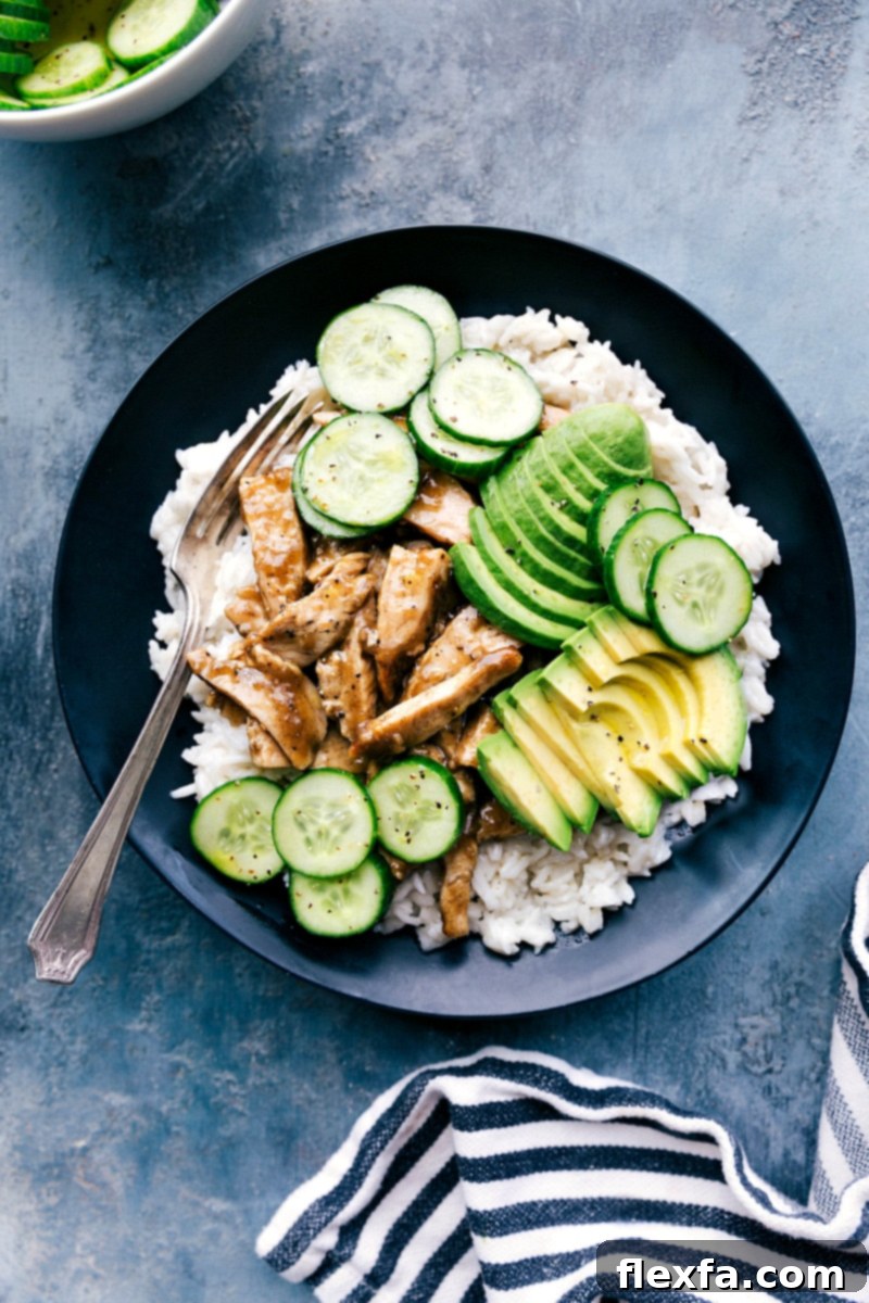 A vibrant bowl of apricot chicken served with fluffy coconut rice, fresh avocado slices, and crisp cucumber salad, ready to be enjoyed.