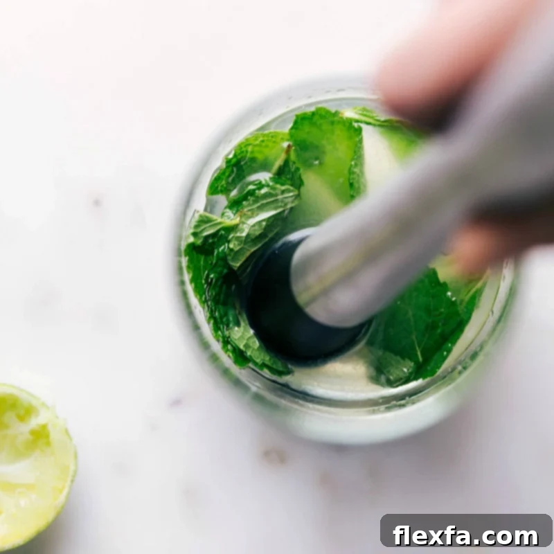 Mint leaves being gently muddled in a glass, releasing their fragrant oils for a refreshing drink.