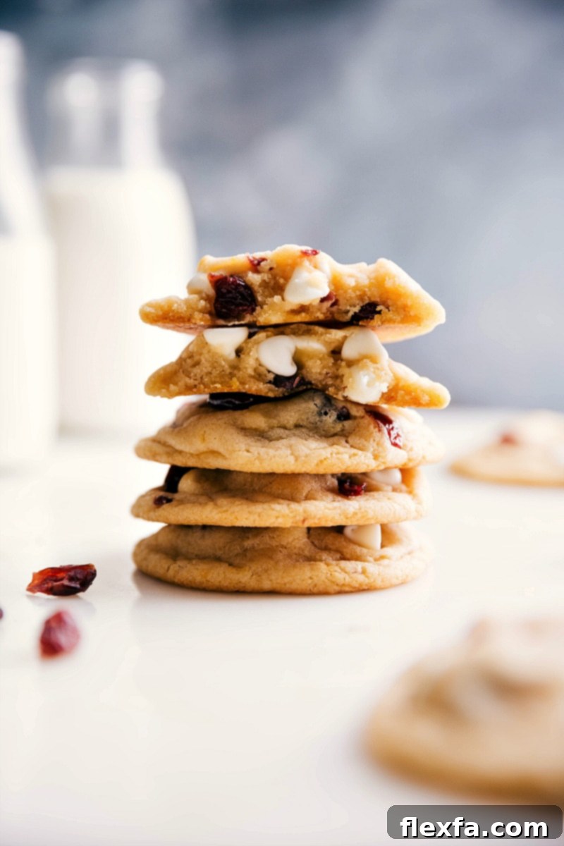 White Chocolate Cranberry Cookie Bliss: A Warm, Gooey Interior Unveiled A beautifully arranged stack of freshly baked white chocolate cranberry cookies, with one cookie expertly broken in half to reveal its warm, gooey interior generously studded with melted white chocolate chips and bright red dried cranberries.
