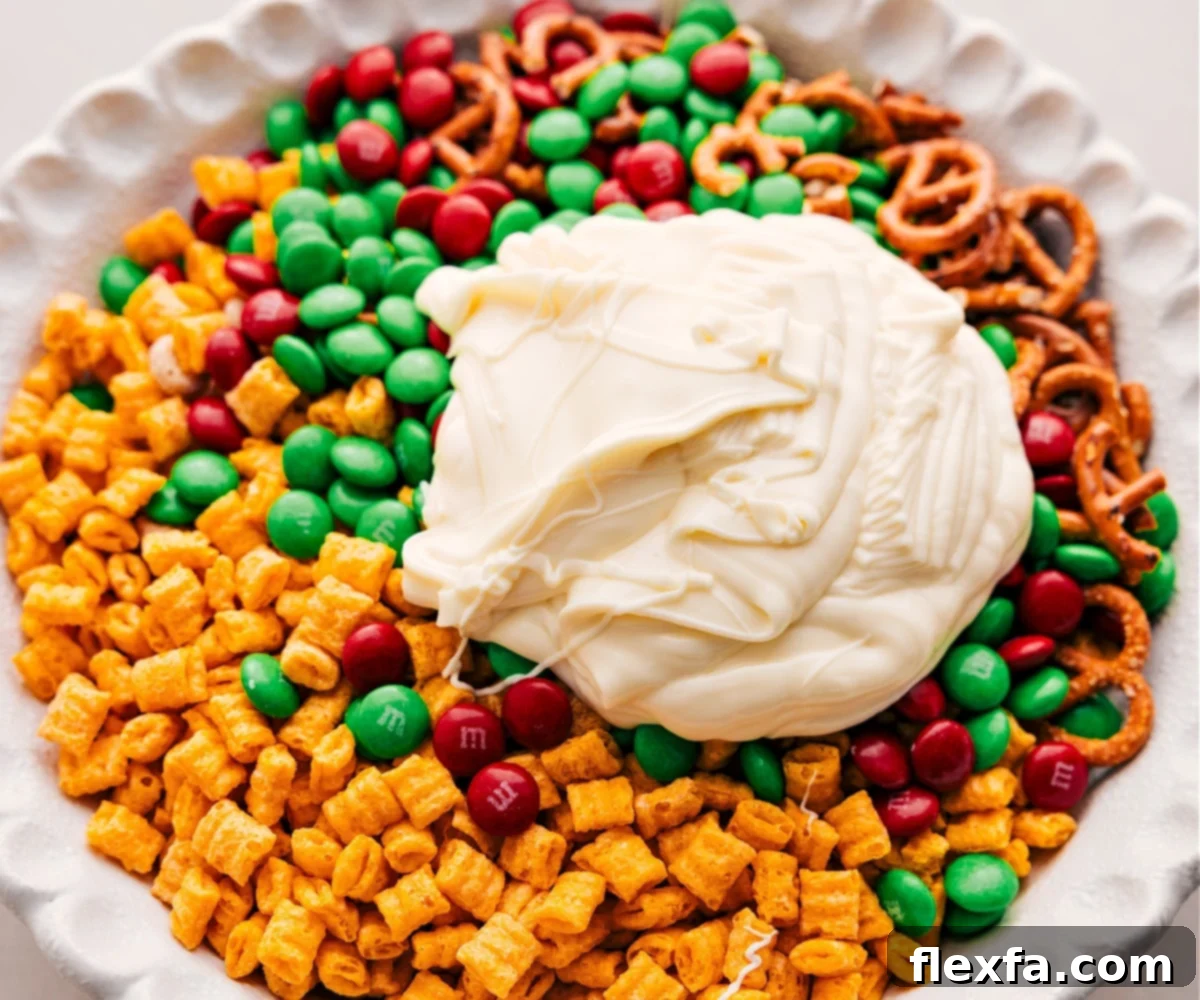 Pouring melted white chocolate over a bowl of dry snack mix ingredients, ready to be coated.