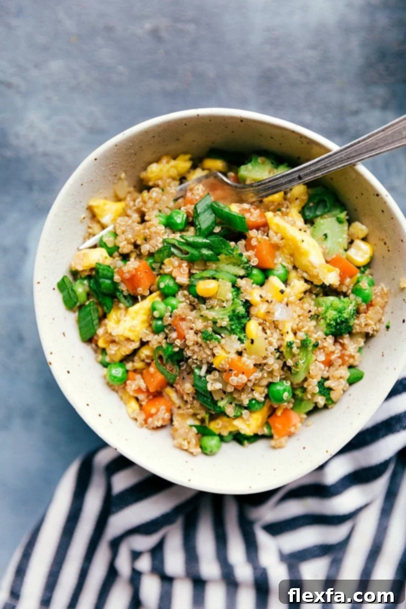 A vibrant bowl of Quinoa Fried Rice, showcasing colorful vegetables like peas, carrots, and corn, with fluffy scrambled eggs and a garnish of green onions, ready to be served.