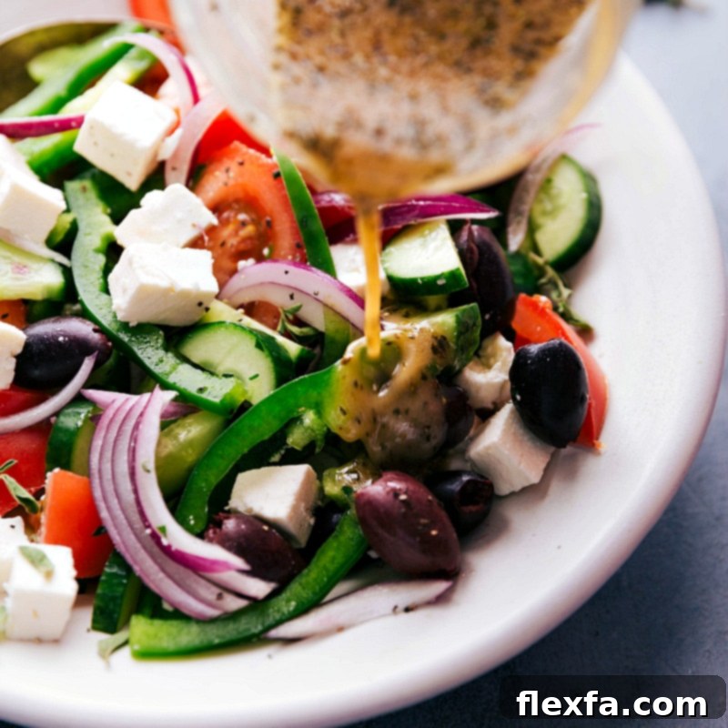 Delicious homemade Greek dressing being poured over a healthy and vibrant Greek salad, showcasing the final step of preparation.