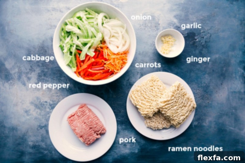 Assortment of fresh ingredients for egg roll noodle recipe, including shredded cabbage, vibrant red bell pepper, thinly sliced onion, matchstick carrots, quick-cooking ramen noodles, ground pork, aromatic garlic, and fresh ginger.