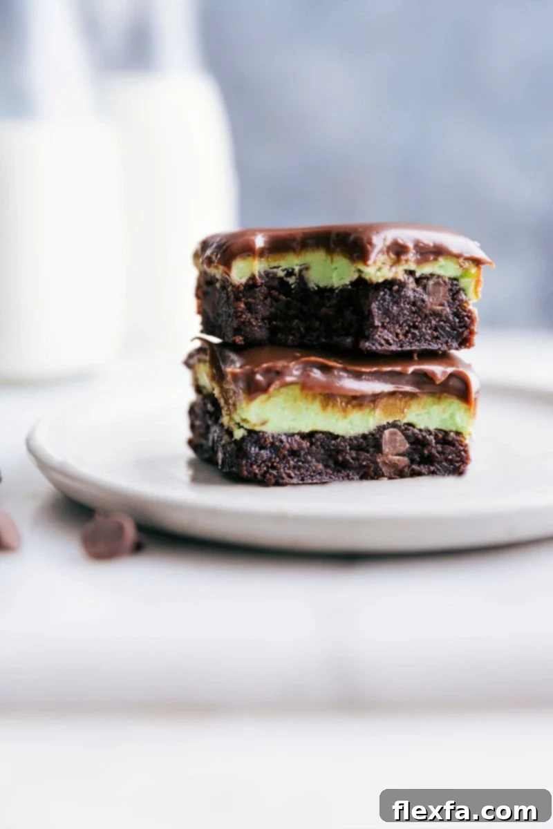 Stacked squares of mint brownies with a bite taken out of the top one, showcasing the mint frosting and chocolate ganache layers.
